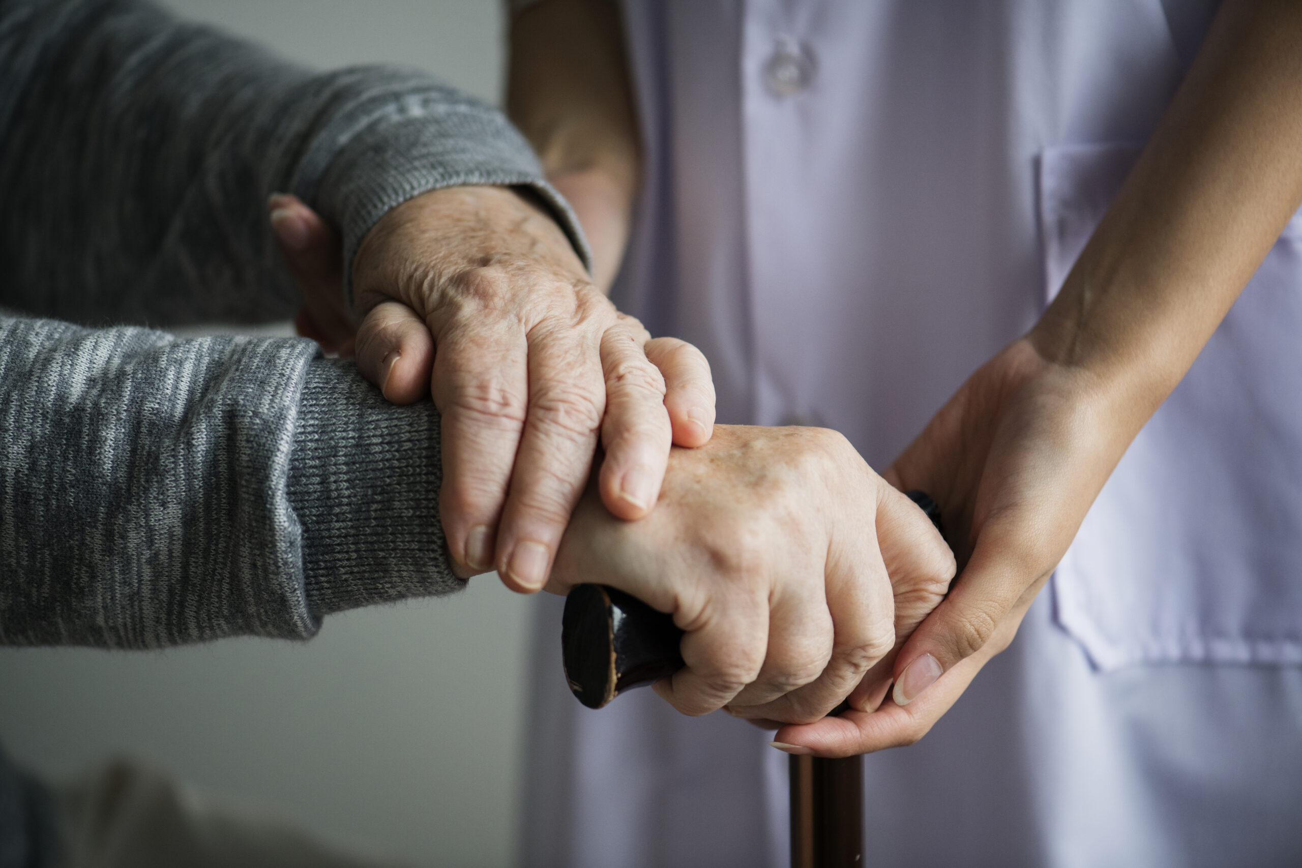 elderly hands being offered support by caregiver to grip cane.