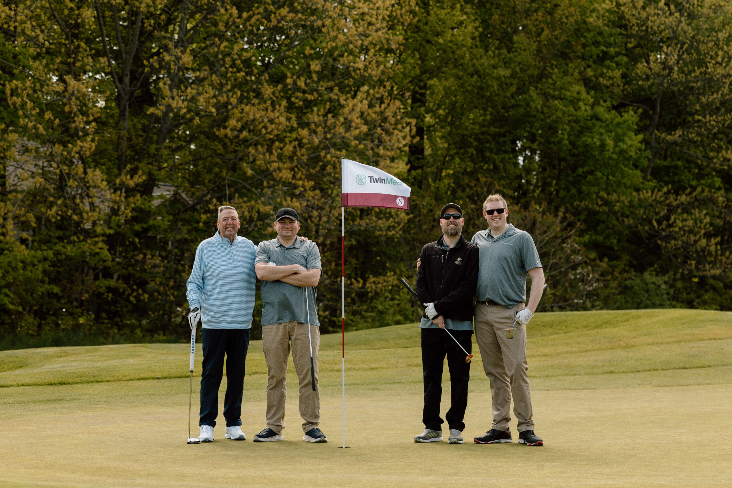 Men golfing and standing on putting green with branded  golf flag. 