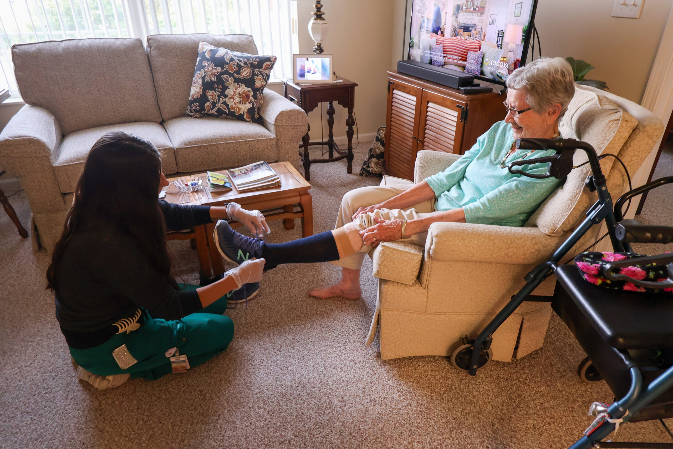 Sunset at Home Visit 2026 Image of caregiver assisting elderly woman with putting socks and shoes on.
