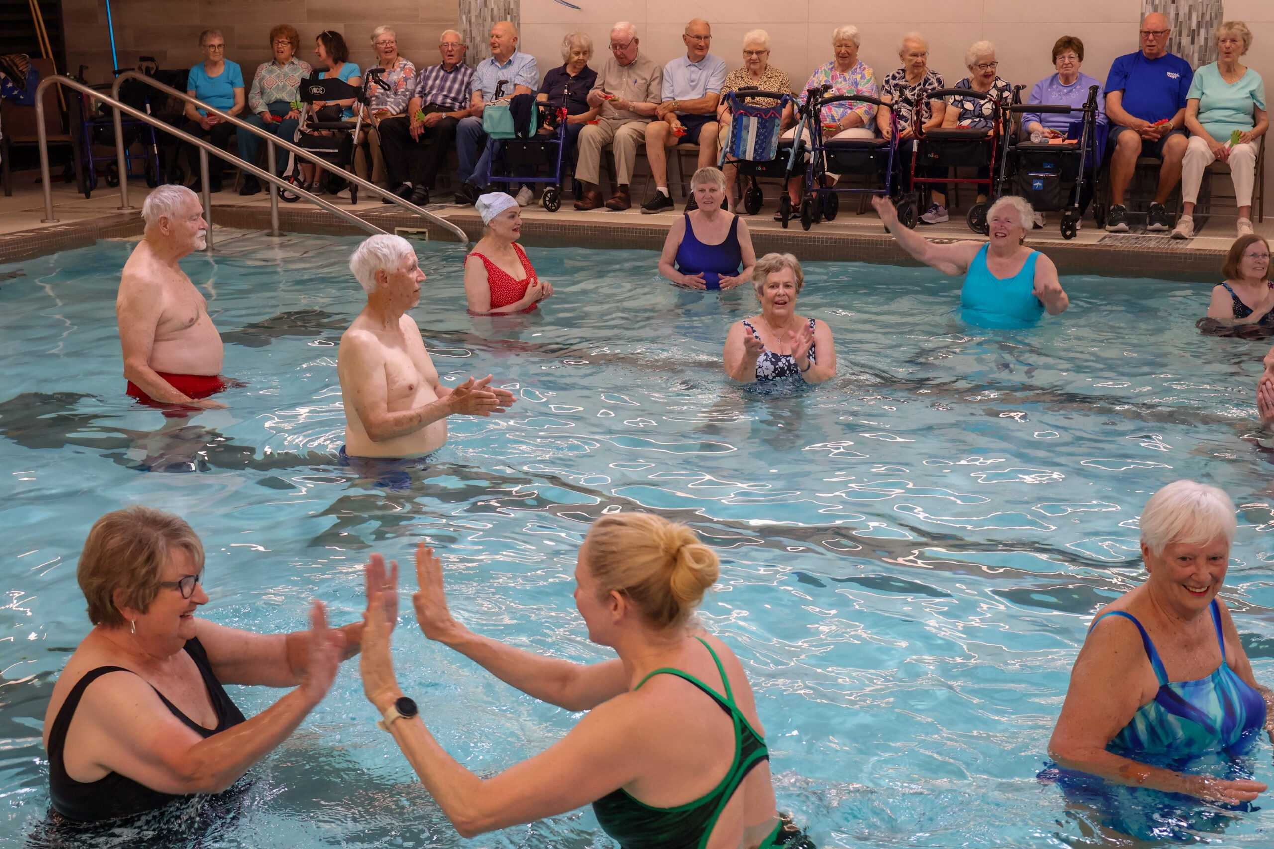 Pool Volleyball 2026 Image of a group of seniors inside an indoor pool playing volleyball. Two people high-fiving each other.