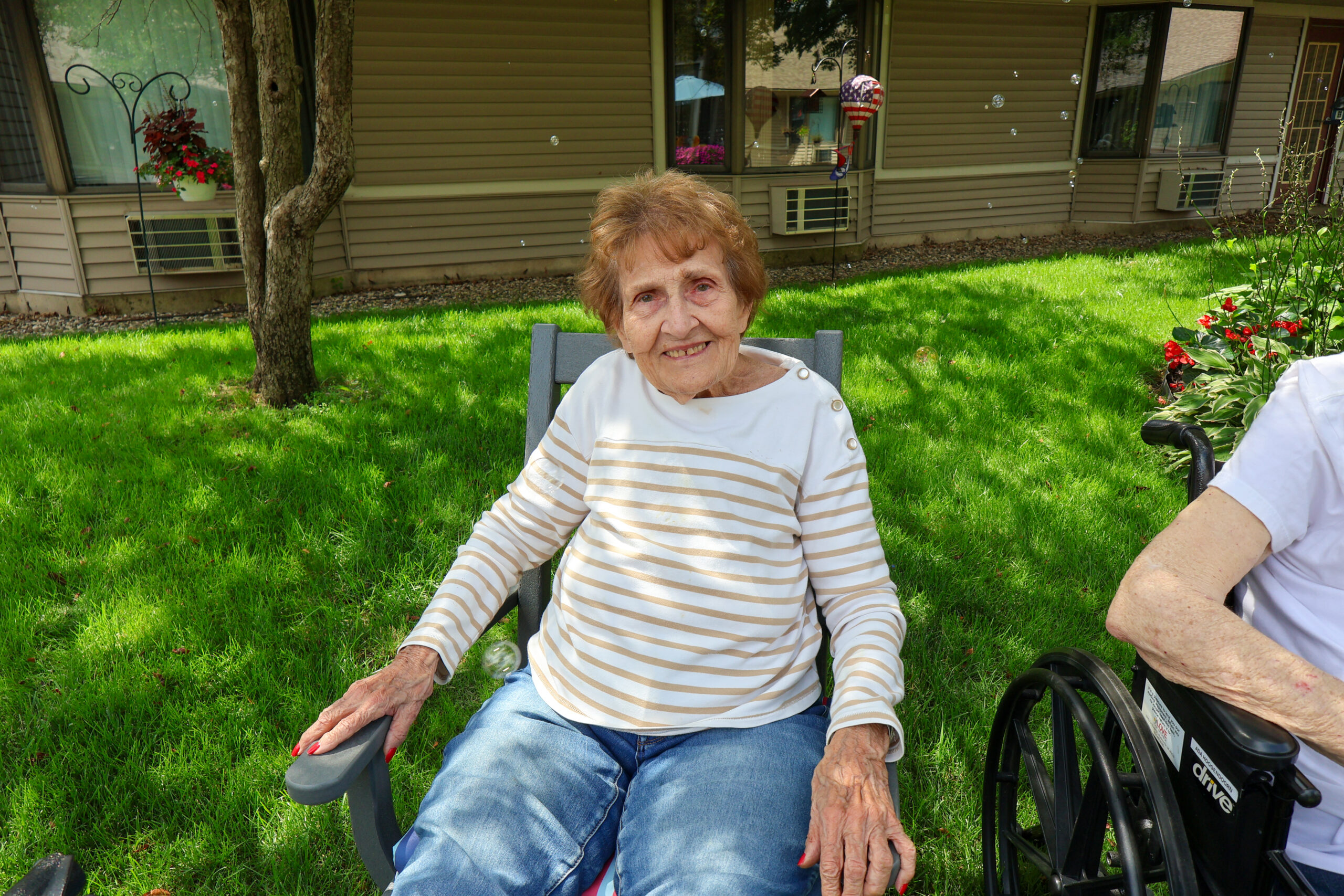 Older woman sitting in a chair outdoors, smiling.